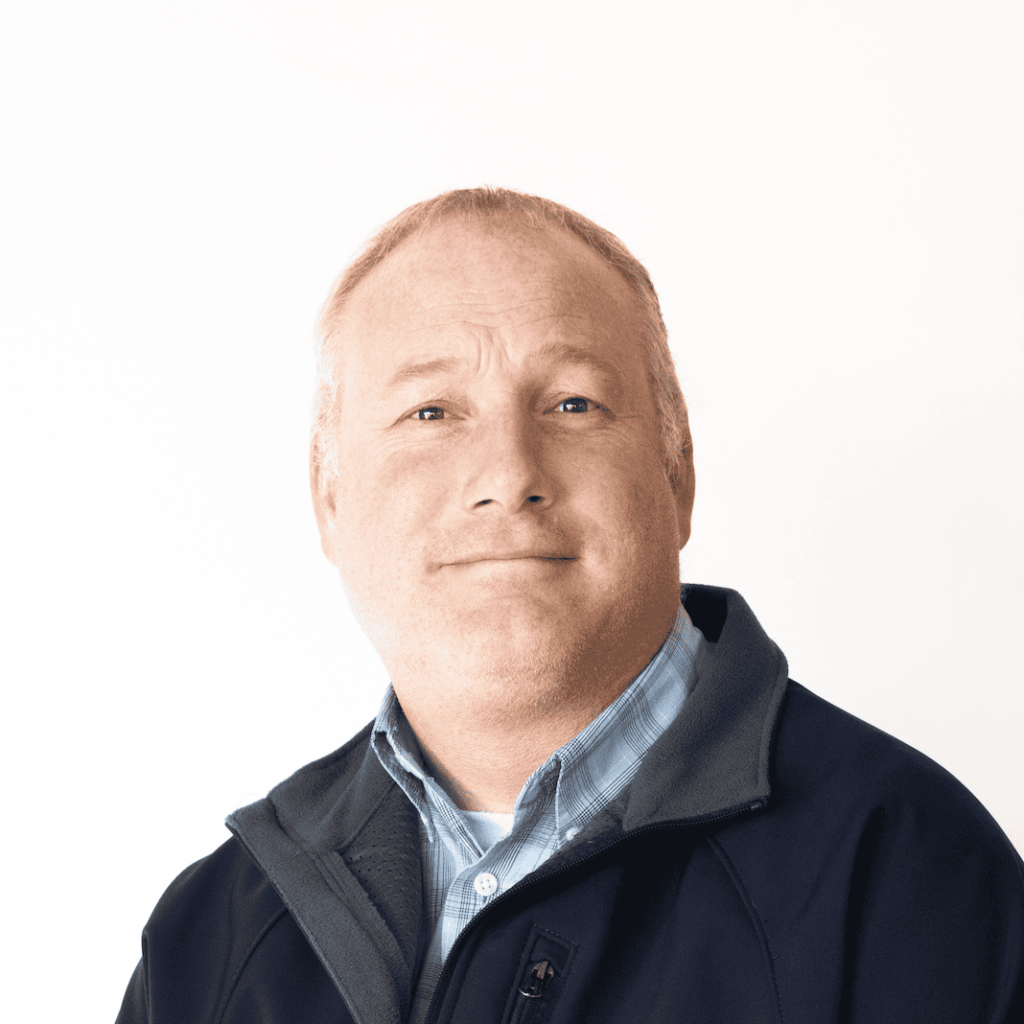 Professional headshot of Brad Clayson, Bingham Ag Services team member, wearing a dark jacket over a blue collared shirt