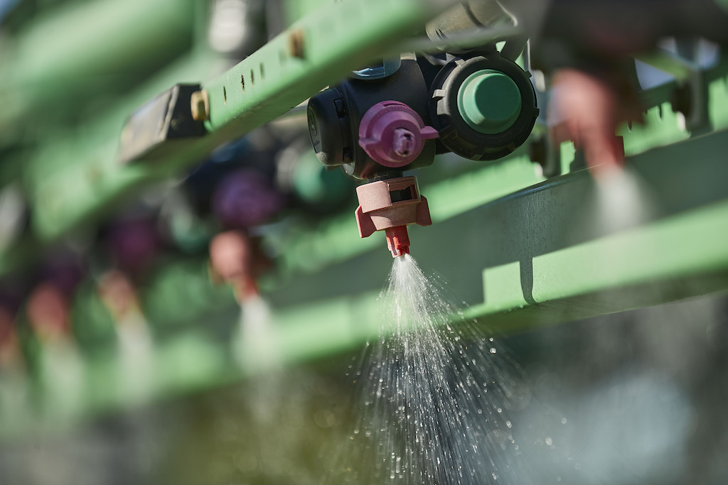 Close-up of agricultural sprayer nozzle actively dispensing liquid insecticide onto crops